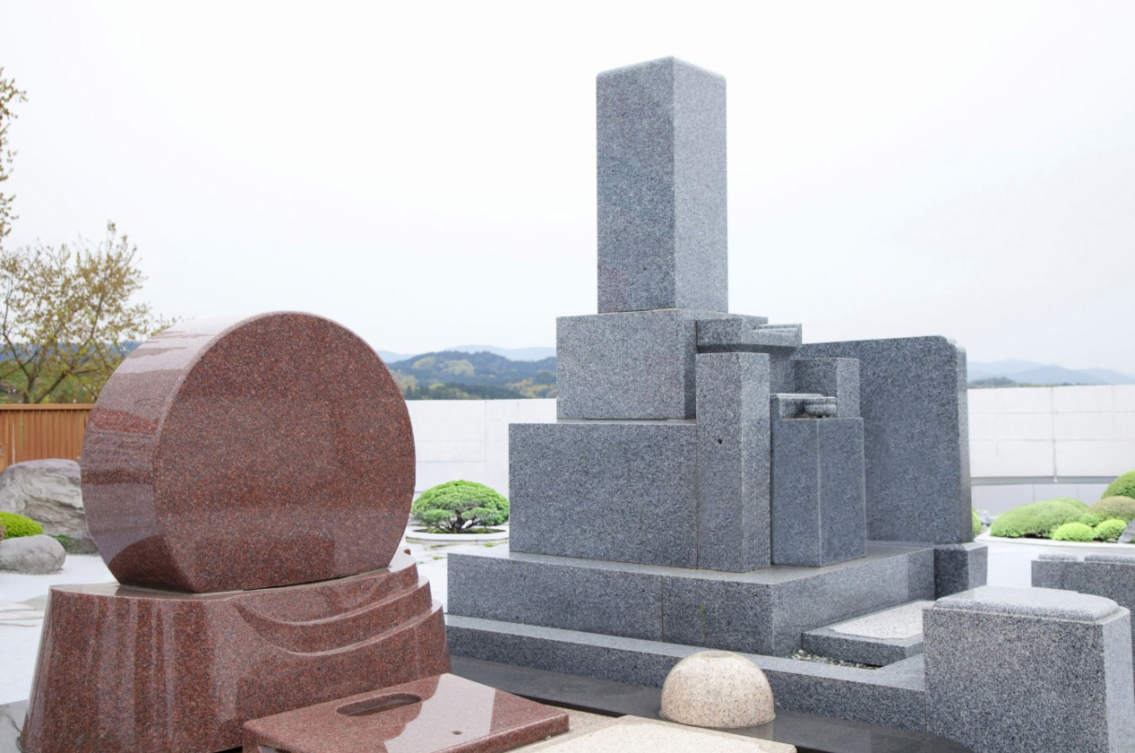 Outdoor stone memorial sculptures: circular reddish-brown and stacked gray geometric forms, symbolizing Elhasg’s artistry and emotional tribute.