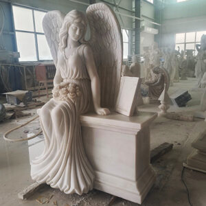 "Life-sized angel headstone monument in white marble, photographed in workshop with sculpted figures and tools."