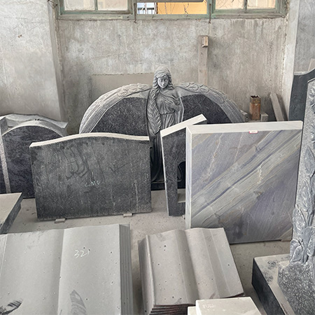 "Black granite headstone with sculpted winged angel, photographed in our factory among other stone components and tools."