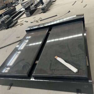 "Polished double ledger memorial made of black granite, photographed in workshop with tools and granite slabs."