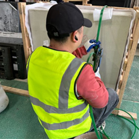 "ELHASG technician in safety gear securing a stone slab with green strapping inside a wooden crate for international shipment."