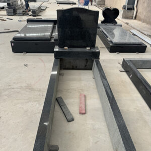 "Granite headstones, full ledgers, and kerb set components in various stages of assembly, photographed inside ELHASG workshop with tools and stone slabs."