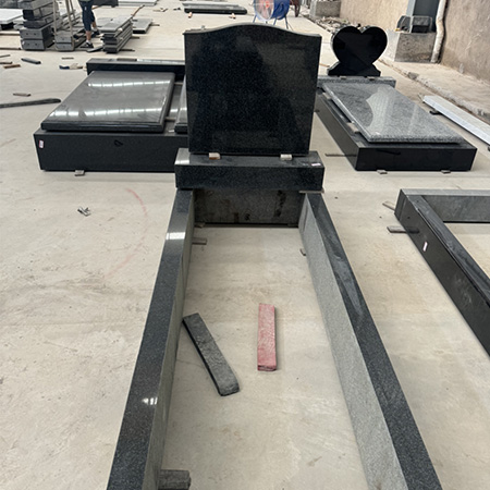 "Granite headstones, full ledgers, and kerb set components in various stages of assembly, photographed inside ELHASG workshop with tools and stone slabs."