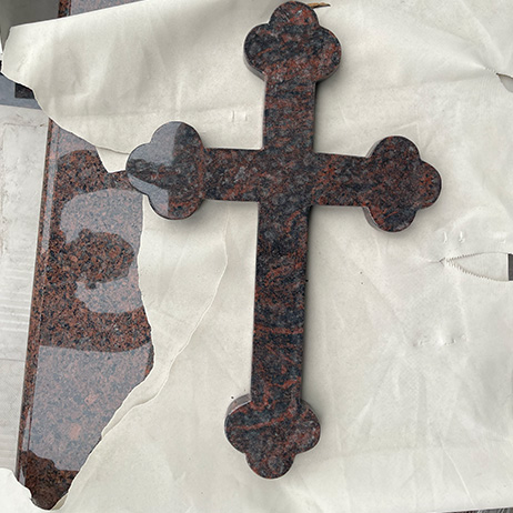 "Polished granite ledger top with sculptural cross element in dark red and black stone, photographed in ELHASG factory on protective fabric."