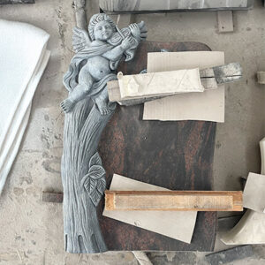"Hand-carved headstone memorial sculpture of angel playing violin within tree trunk, photographed in workshop with tools and materials."
