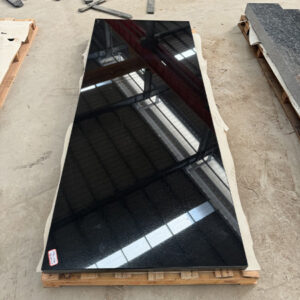 "Polished single ledger memorial made of black granite, photographed in workshop with stone slabs and pallet."