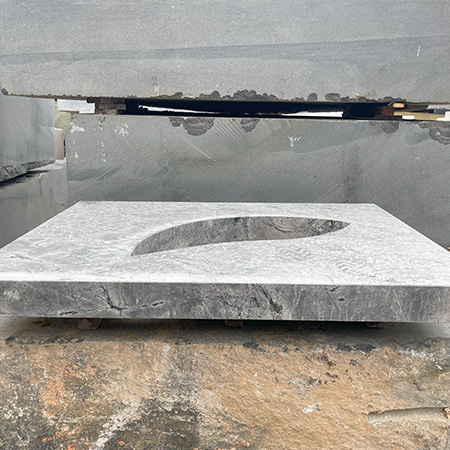 "Handcrafted granite ledger memorial with recessed teardrop cutout, photographed in workshop with tools and raw stone slabs."