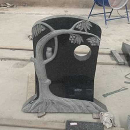 "Granite memorial slab with carved tree design and circular cutout, standing upright in ELHASG workshop surrounded by tools and stone blocks."