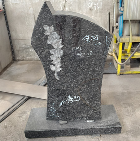 "Unfinished granite headstone with floral engraving and matching base, photographed in our factory surrounded by tools and materials."