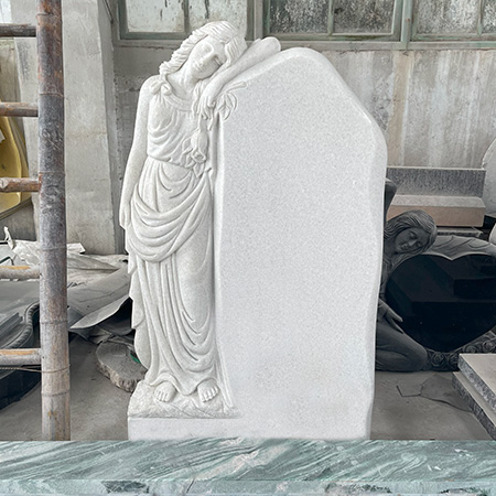 "Unfinished marble memorial headstone with sculpted angel resting peacefully on blank panel, photographed in our factory surrounded by tools and stone components."