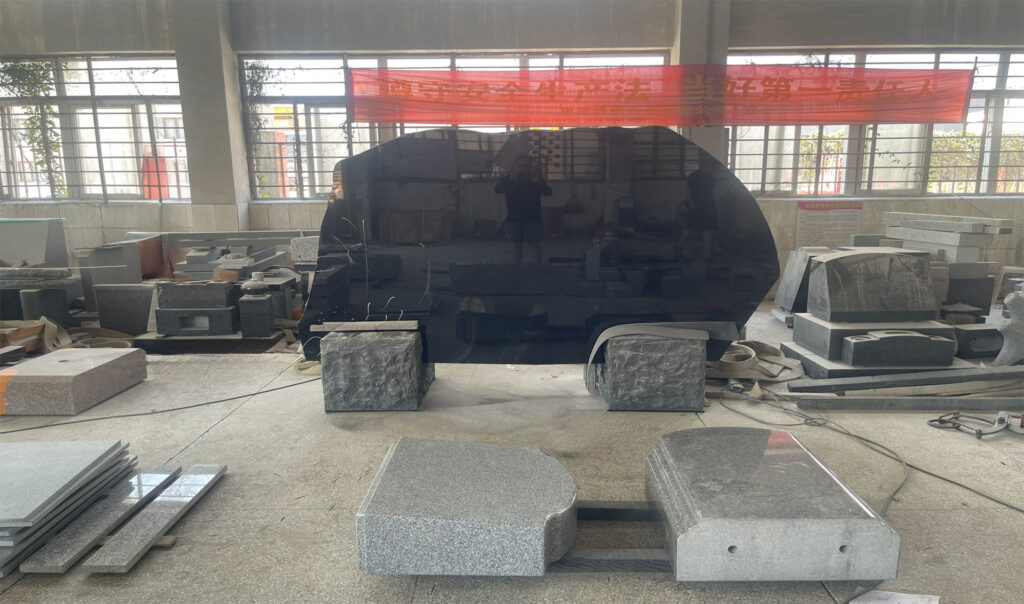 "ELHASG memorial factory interior with polished black granite slab and headstone components, showcasing active stonework and global project scale."