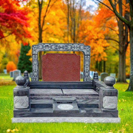 "Polished stone upright headstone with red central plaque, flanked by decorative pillars with spherical tops, mounted on a multi-tiered stone base."