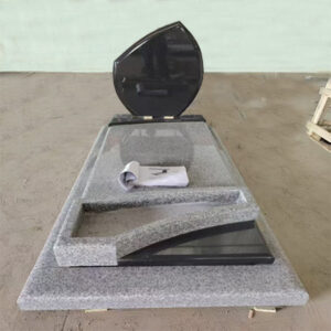 "Polished granite upright headstone in asymmetrical black form with layered grey ledger and curved cutout."