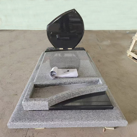 "Polished granite upright headstone in asymmetrical black form with layered grey ledger and curved cutout."