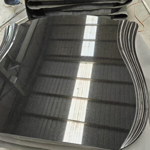 "Polished black granite slabs with sculpted edge design in batch production at Elhasg factory."