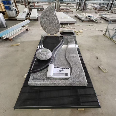 "Black and grey polished granite upright headstone with leaf-shaped design and wave-contoured ledger base."