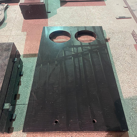 "Polished granite ledger tombstone cover with twin circular cutouts in Elhasg workshop surrounded by stone blocks."