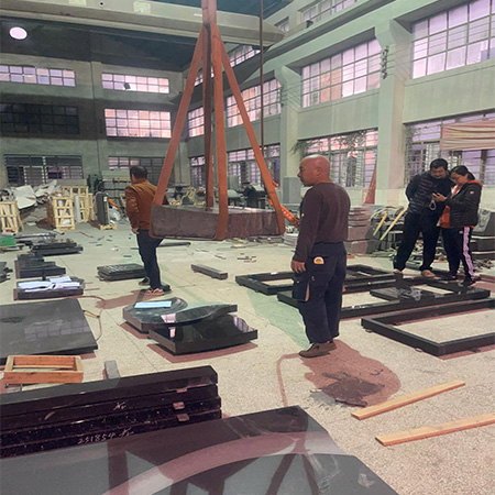 "Granite slab lifted by crane in Elhasg factory with workers and stone components for headstone projects."
