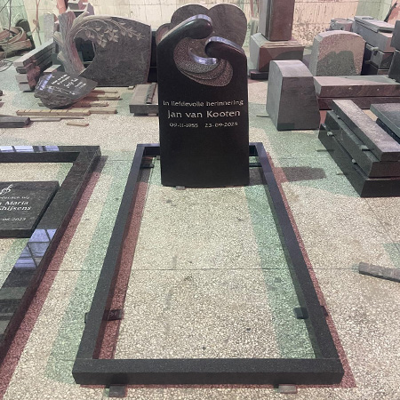 "Granite headstone with sculpted top and kerb set in Elhasg workshop surrounded by memorial components."