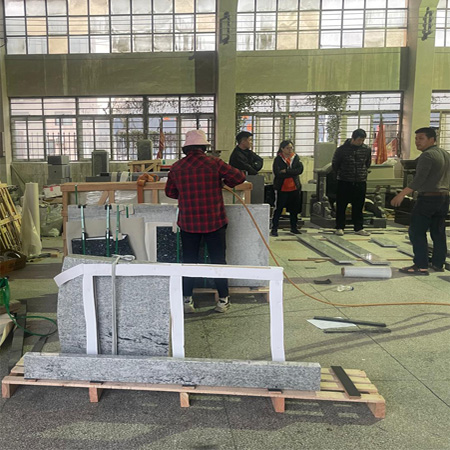 "Gray granite headstone and ledger on pallet with straps and tools in Elhasg factory."