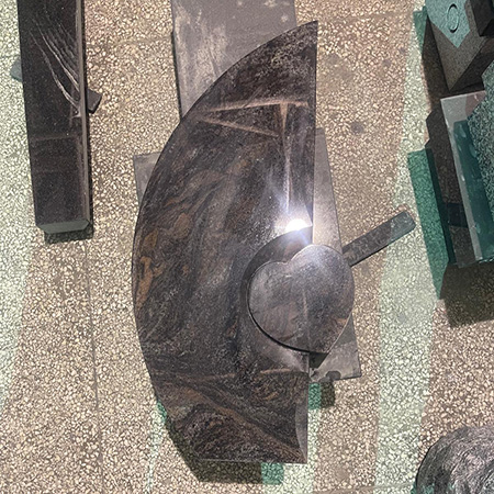 "Polished heart-shaped granite component with circular base surrounded by stone blocks in Elhasg workshop."