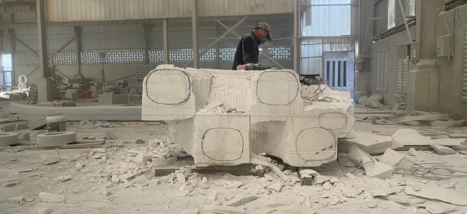 "Artisan marking and shaping marble elephant base in Elhasg workshop with tools and stone debris."