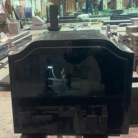 "Polished black granite monument with curved top on sawhorses in Elhasg workshop surrounded by stone slabs and tools."