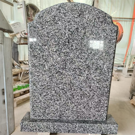 "Speckled granite headstone with rounded top and polished surface on rectangular base at Elhasg workshop."