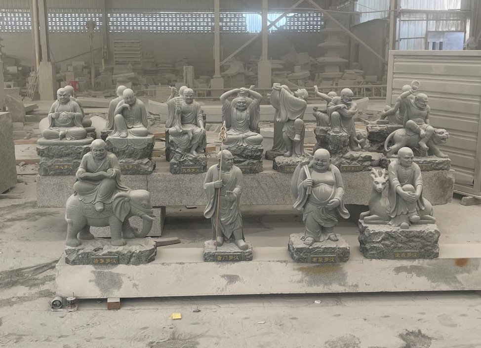 "Seated Arhat statues on inscribed bases in Elhasg workshop with tools and stone slabs."