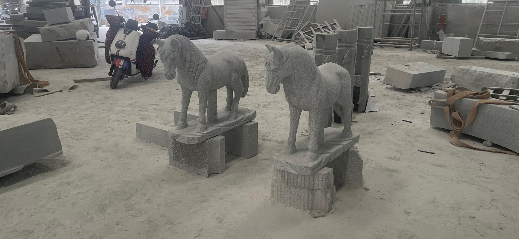 "Stone horse sculptures on blocks in Elhasg workshop surrounded by tools, slabs, and equipment."