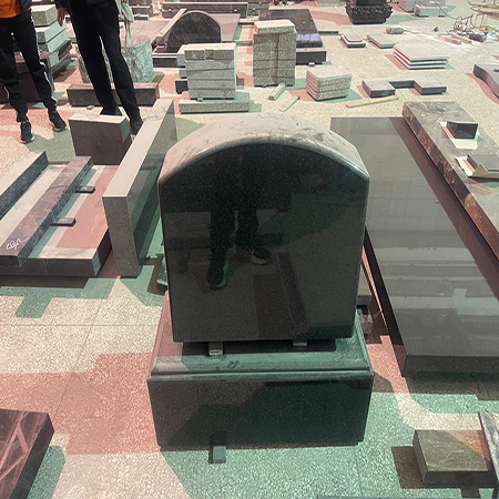 "Polished black granite upright headstone with curved top in Elhasg workshop surrounded by stone slabs."