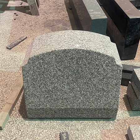 "Polished gray granite upright headstone with rounded top in Elhasg workshop surrounded by stone slabs."